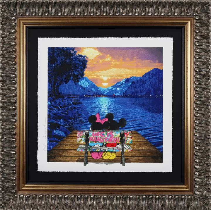 A Mr Brainwash framed limited edition of Mickey and Minnie Mouse sat on a bench overlooking a lake and mountains at sunset, the title is A World Full of Wonder