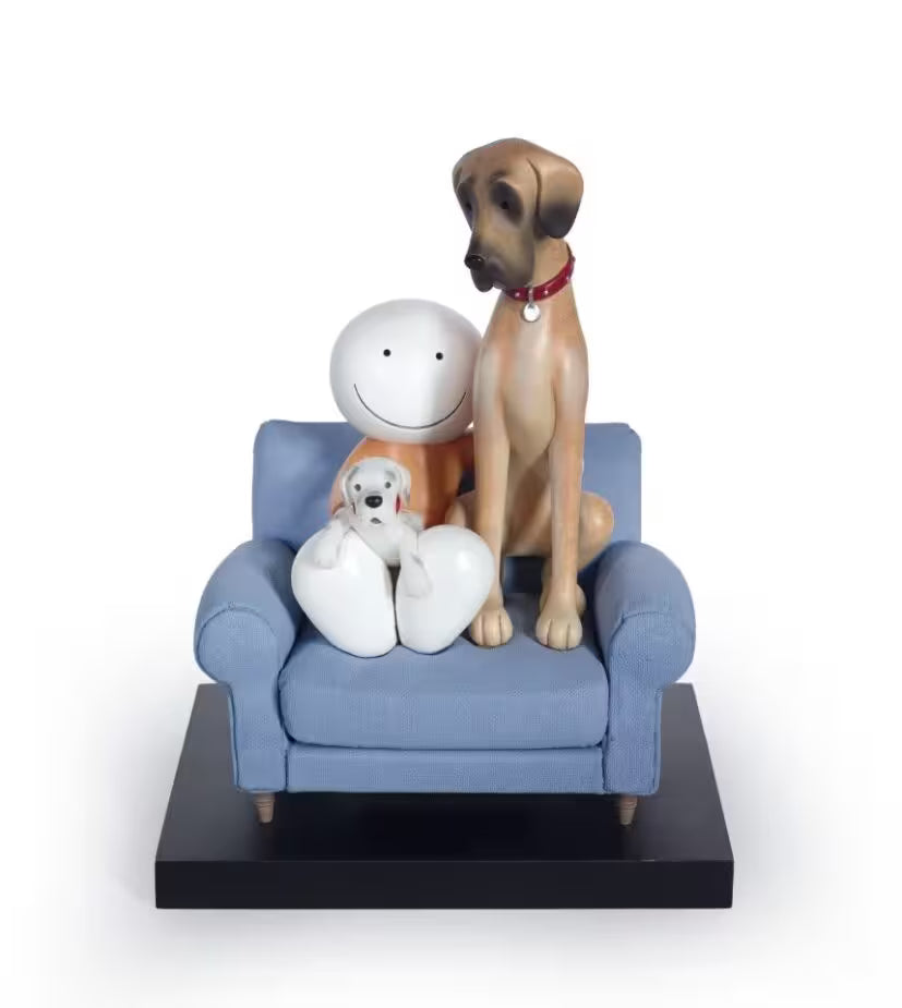 A sculpture by Doug Hyde of a larger dog sitting next to a smaller dog on a blue sofa, with a white base and a red collar on the larger dog, title is Always by your Side
