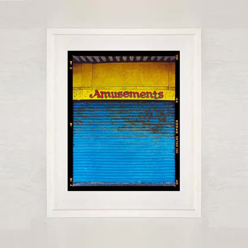 A white framed limited edition photograph by Richard Heeps using vibrant colours, the title is Amusements, Porthcawl, 2023