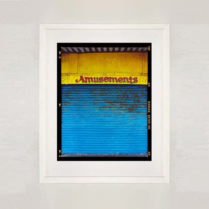 A white framed limited edition photograph by Richard Heeps using vibrant colours, the title is Amusements, Porthcawl, 2023