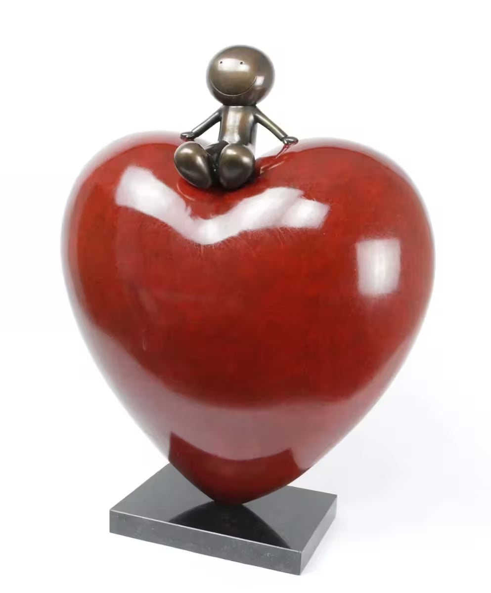 A bronze sculpture by Doug Hyde of a person sat on top of a big red heart, title is Big Love (Deluxe)