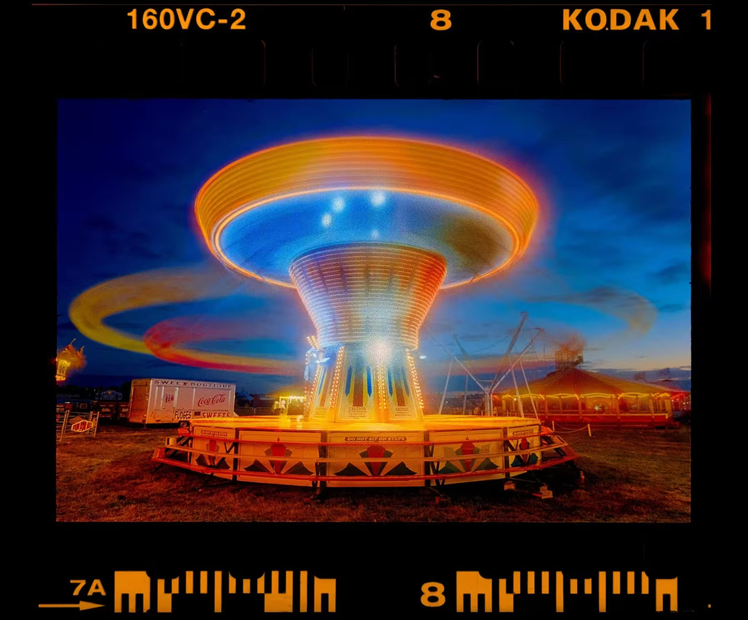 A limited edition photograph by Richard Heeps using vibrant colours, the title is Chair-O-Planes Going Round, Haddenham Steam Rally, Cambridgeshire, 2019