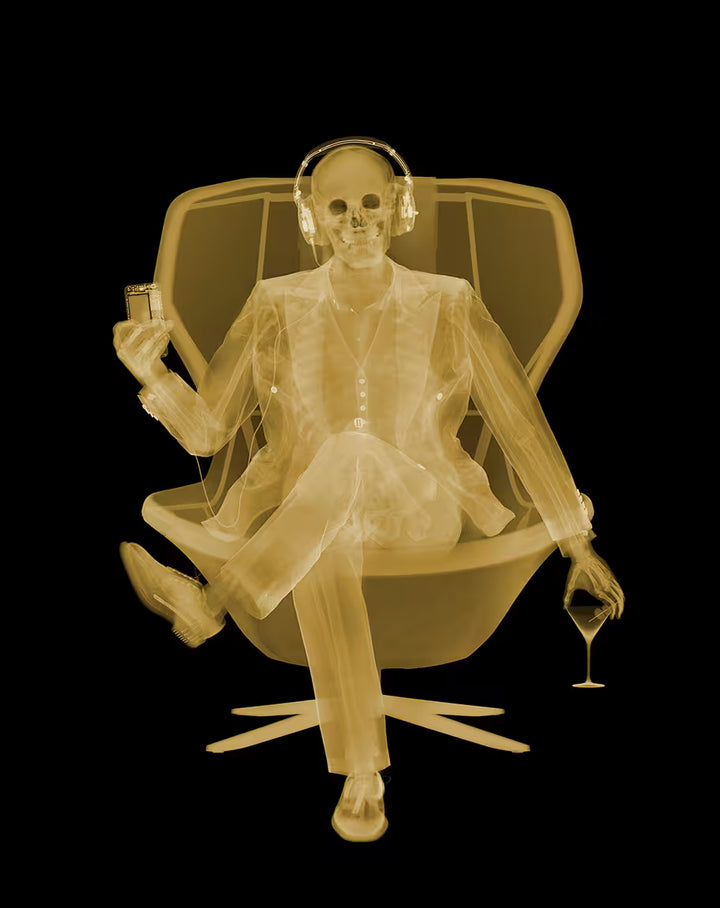 A Nick Veasey limited edition Chromaluxe Xray of a person sat in a chair drinking with headphones on listening to music, the title is Easy Listener- Golden Era