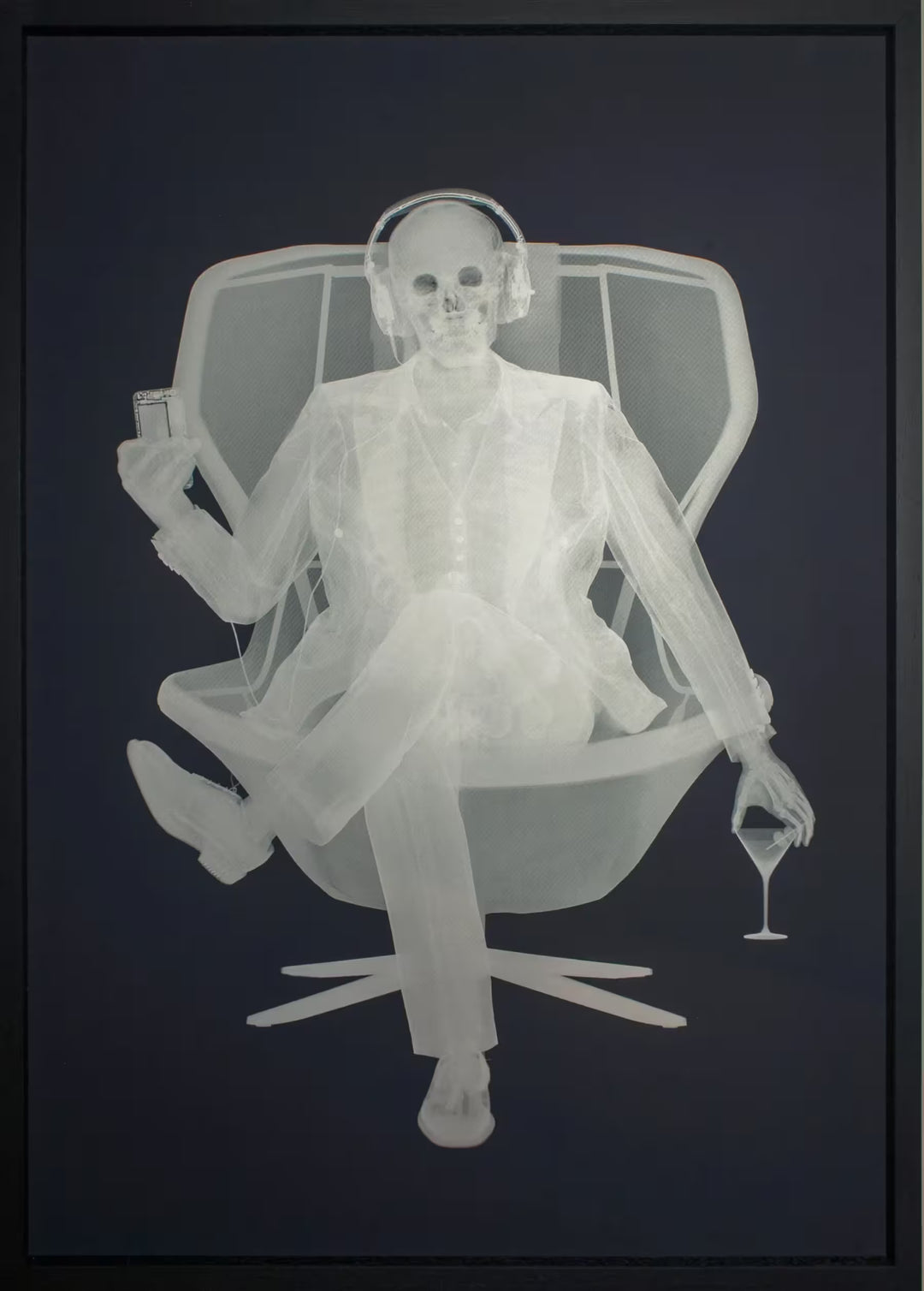 A limited edition framed Silkscreen print by Nick Veasey of an X-Rayed skeleton sat on a chair in a suit, they are wearing headphones connected to the device they are holding, the title is Easy Listener