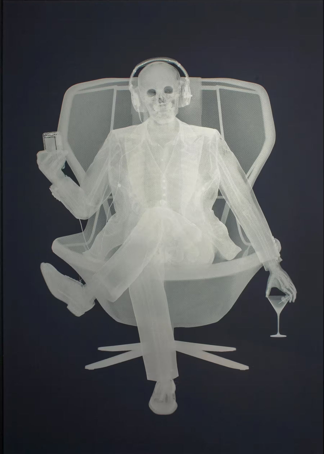 A limited edition Silkscreen print by Nick Veasey of an X-Rayed skeleton sat on a chair in a suit, they are wearing headphones connected to the device they are holding, the title is Easy Listener