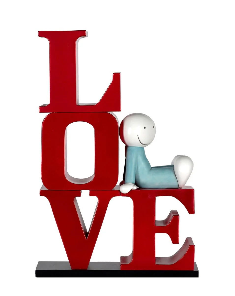 A sculpture by Doug Hyde of the word Love in the shape of the letter L, a person wearing blue is sitting on top of the letter E, the title is Happy In Love 