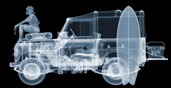 A limited edition Chromaluxe print by Nick Veasey of an X-Rayed vehicle with a skeleton person sat on the front of the car along with beach items scattered around the car, the title is Land Rover- After Surf