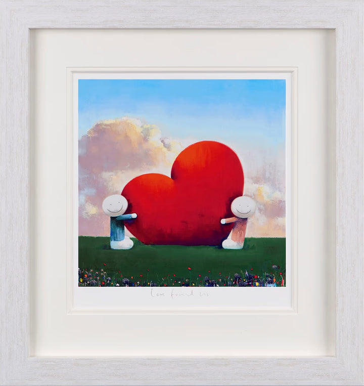 Framed artwork of two figures holding a large red heart against a colourful sky, Love Found Us by Doug Hyde