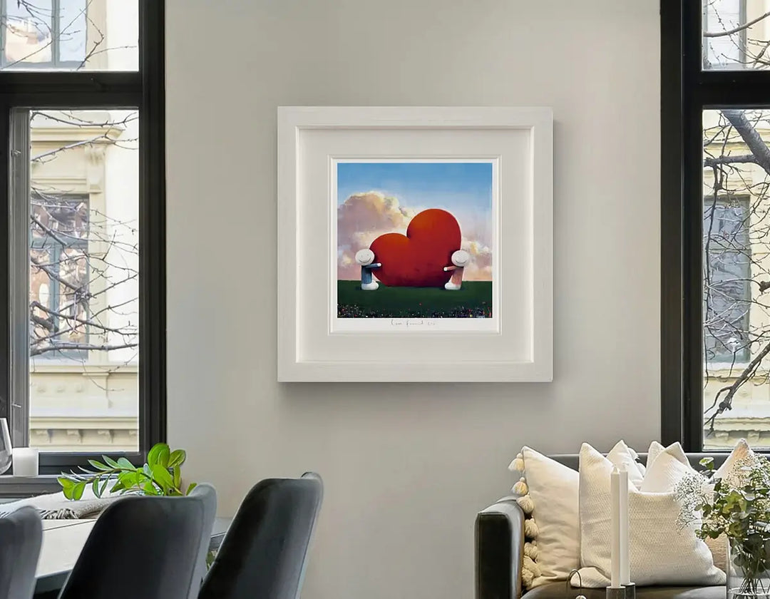 Framed artwork of a red heart with white wings on a wall in a living room, Love Found Us by Doug Hyde