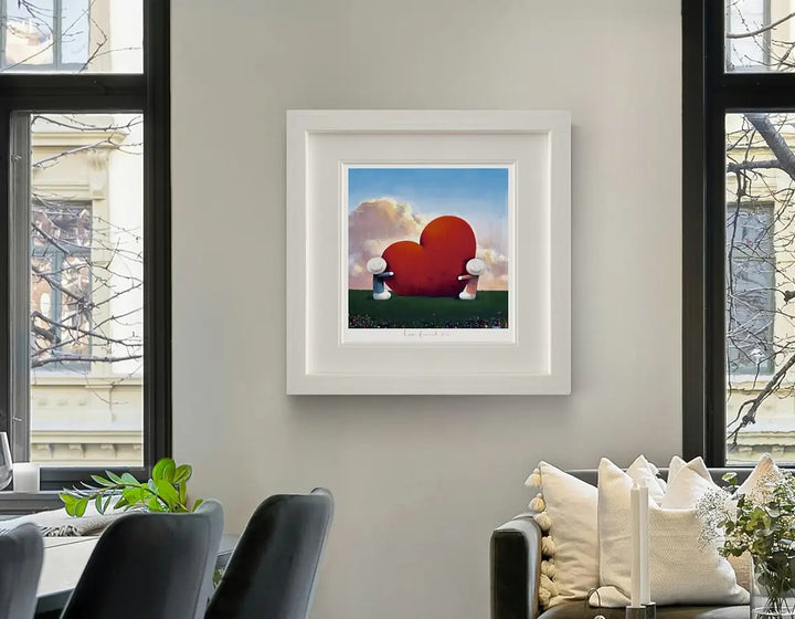 Framed artwork of a red heart with white wings on a wall in a living room, Love Found Us by Doug Hyde