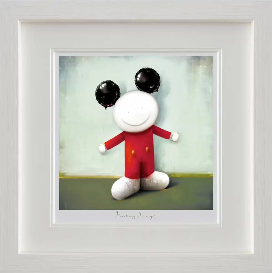 A Doug Hyde framed limited edition of a person wearing red with two yellow buttons on their clothes and holding two black balloons to resemble ears, the title is Making Magic