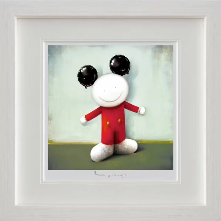 A Doug Hyde framed limited edition of a person wearing red with two yellow buttons on their clothes and holding two black balloons to resemble ears, the title is Making Magic
