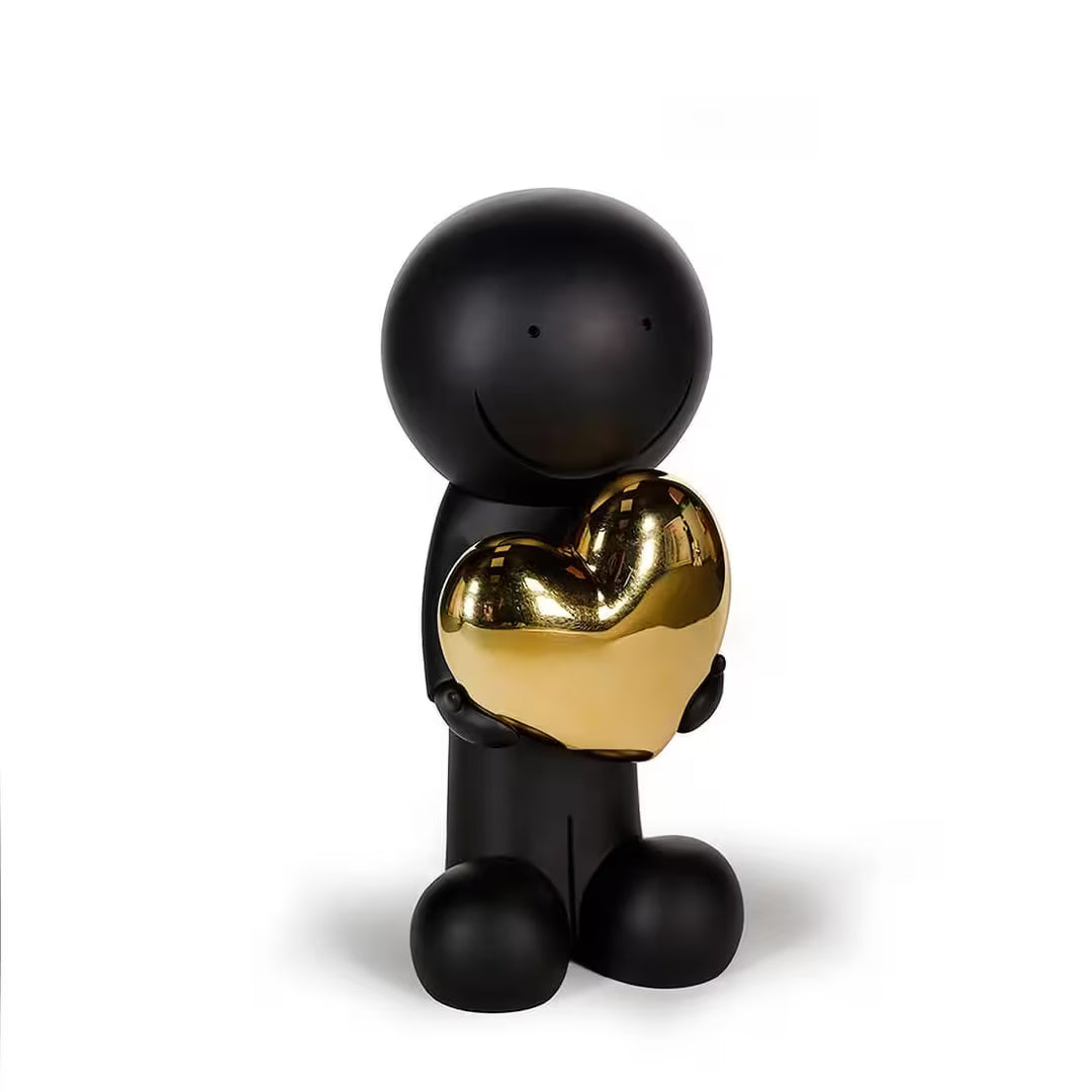 A sculpture by Doug Hyde of a person holding a heart in black and gold, the title is One Love (Black & Gold)