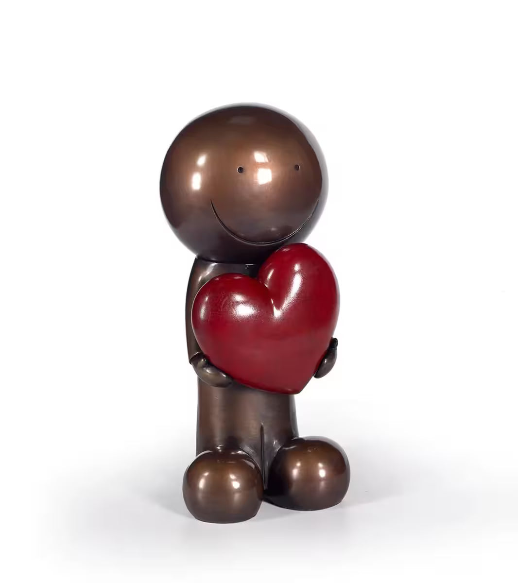 A sculpture by Doug Hyde of a bronze person holding a red heart, the title is One Love