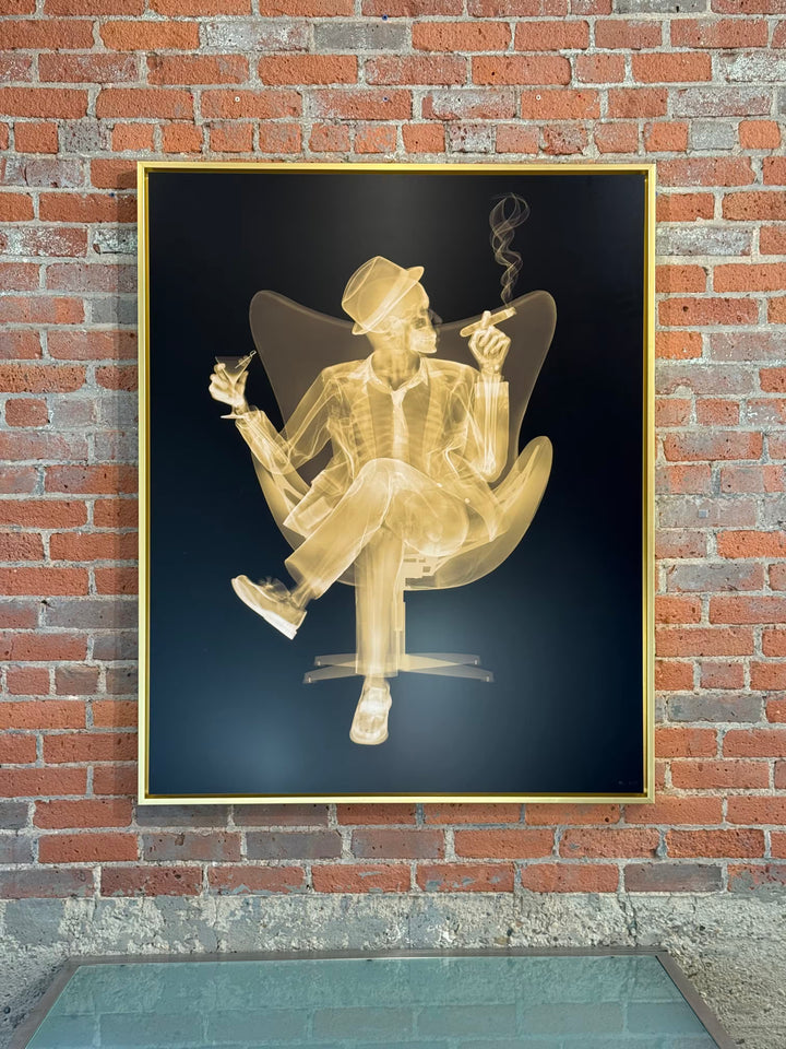 A Nick Veasey limited edition Chromaluxe X ray of a person sat in a chair drinking and smoking a cigar, the title is Rat Pack II- Golden Era