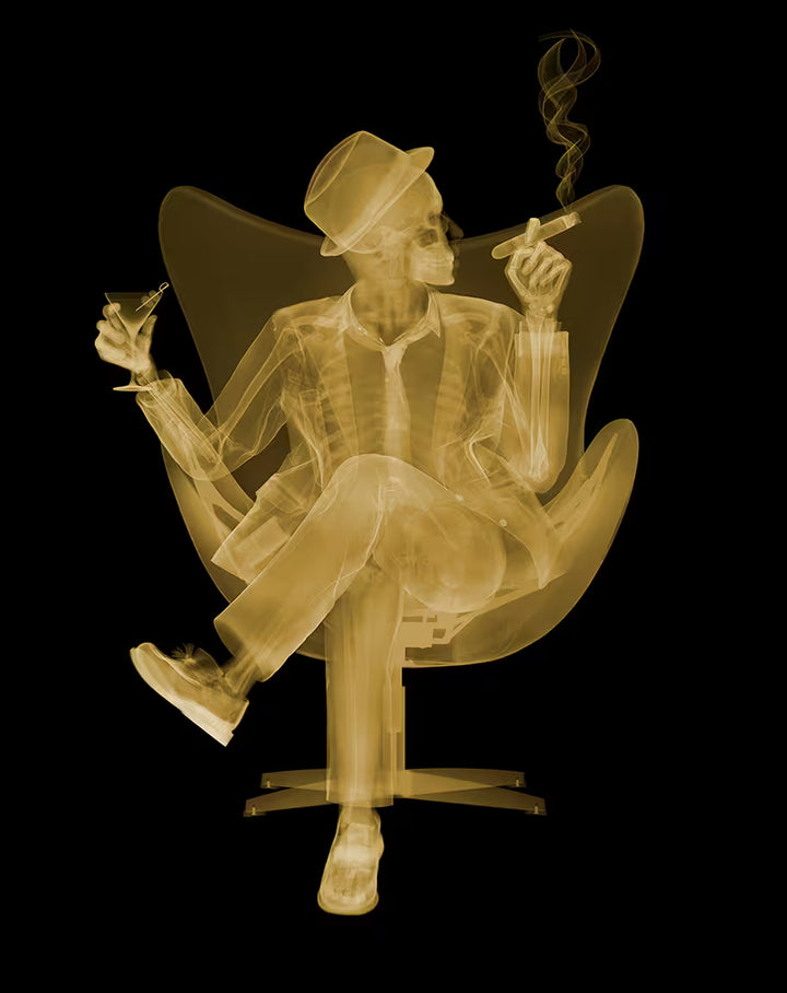 A Nick Veasey limited edition Chromaluxe X ray of a person sat in a chair drinking and smoking a cigar, the title is Rat Pack II- Golden Era