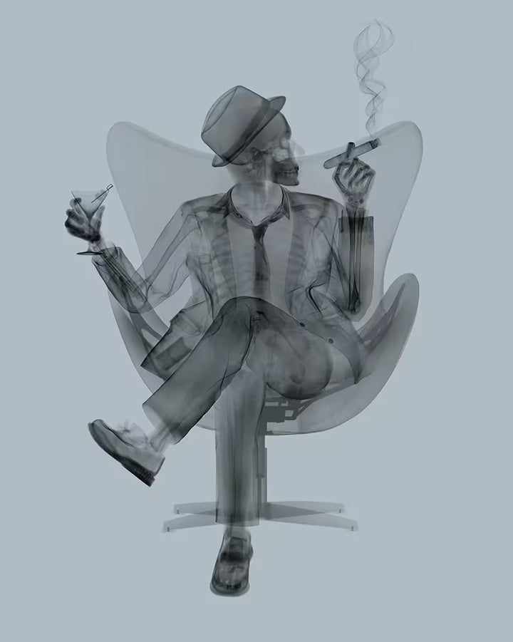 A limited edition Chromaluxe print by Nick Veasey of an X-Rayed ratpack member with a hat on sat on a big chair with a drink in their hand and smoking a cigar, the title is Rat Pack II Grey