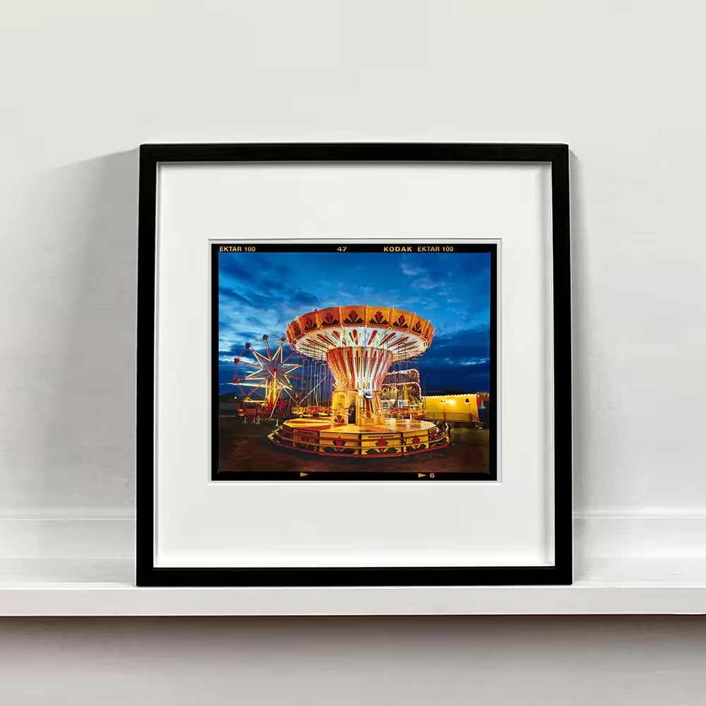 A black framed limited edition photograph by Richard Heeps using vibrant colours, the title is Chairoplanes, Haddenham, 2022