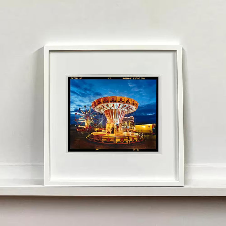 A white framed limited edition photograph by Richard Heeps using vibrant colours, the title is Chairoplanes, Haddenham, 2022