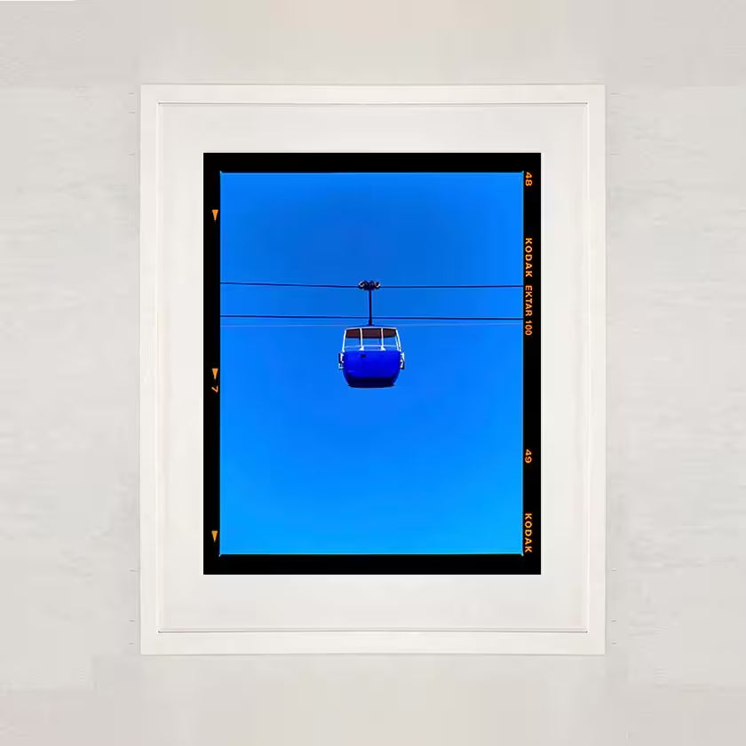 A white framed limited edition photograph by Richard Heeps using vibrant colours, the title is Summit Cable Car (Blue)