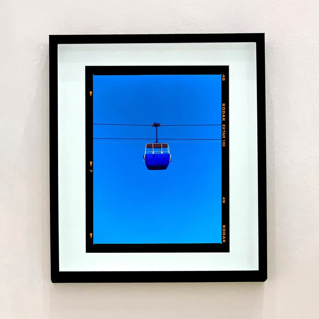 A framed limited edition photograph by Richard Heeps using vibrant colours, the title is Summit Cable Car (Blue)