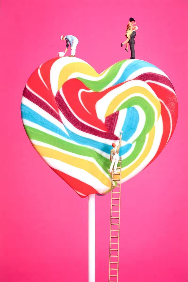 A Mr Kuu limited edition piece of a heart shaped lollipop with people painting the stripes and a couple on top, the title is Sweet Art