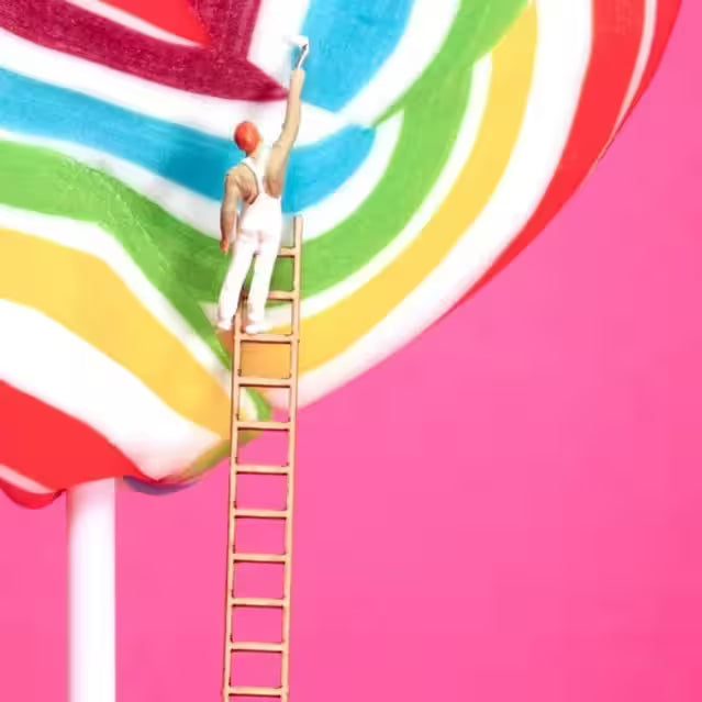 A Mr Kuu limited edition piece of a heart shaped lollipop with people painting the stripes and a couple on top, the title is Sweet Art