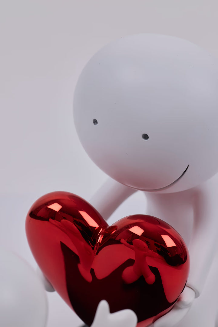 White robot holding a red heart-shaped object against a light gray background, the Greatest Gift by Doug Hyde