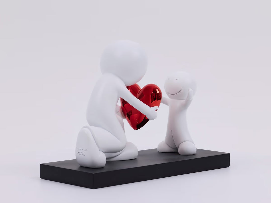 Two white figures holding a red heart on a black platform with a light gray background, the Greatest Gift by Doug Hyde