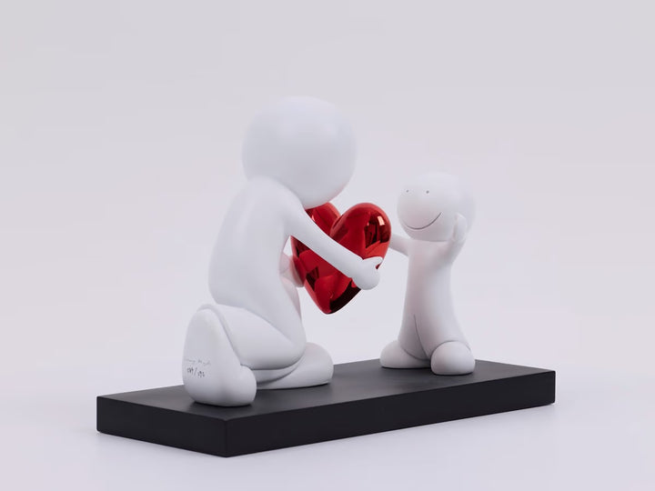 Two white figures holding a red heart on a black platform with a light gray background, the Greatest Gift by Doug Hyde