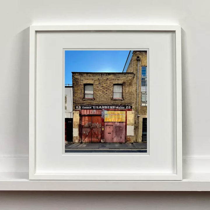 A white framed limited edition photograph by Richard Heeps using vibrant colours, the title is Timber Merchant, London, 2022
