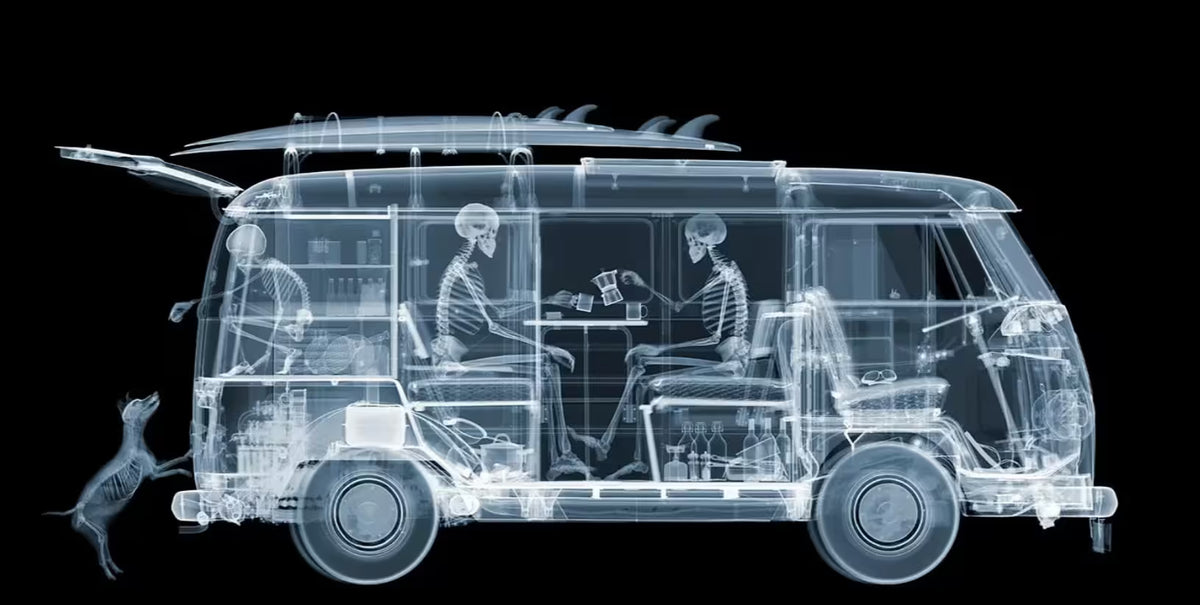 A limited edition Chromaluxe print by Nick Veasey of an X-Rayed vehicle with two skeletonssat inside of it eating and a skeleton dog trying to jump into it, the title is VW Camper Family