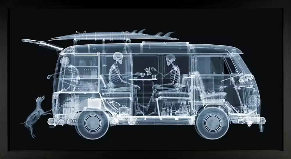 A limited edition framed Chromaluxe print by Nick Veasey of an X-Rayed vehicle with two skeletonssat inside of it eating and a skeleton dog trying to jump into it, the title is VW Camper Family